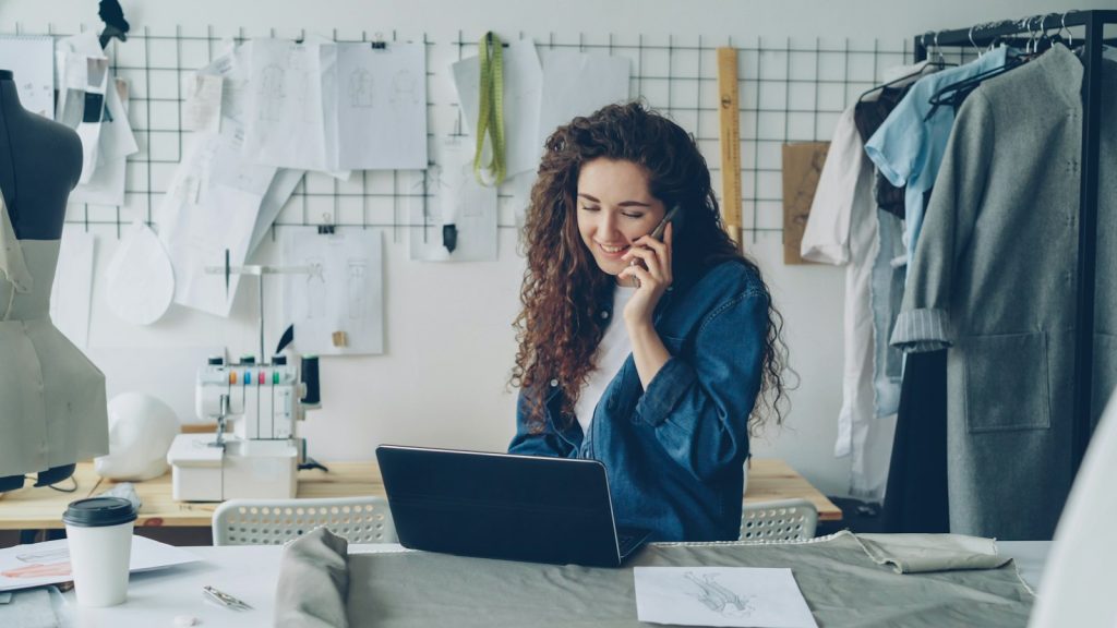 Emprendedora atendiendo a un cliente por teléfono mientras trabaja en su laptop