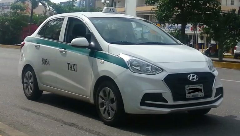 Taxi de Cancún blanco con franja verde en una avenida con palmeras